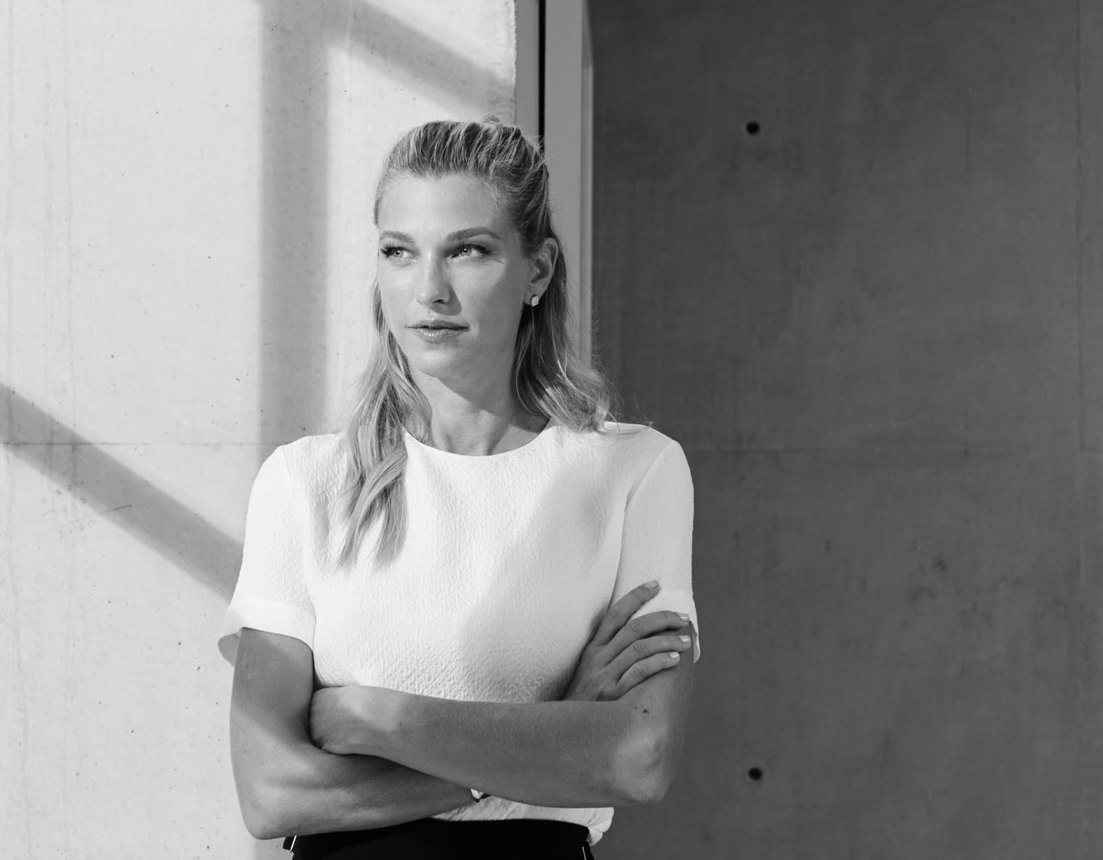 Nicole Junkermann, Schwarz-Weiß-Porträt mit verschränkten Armen vor einer hellen Betonwand